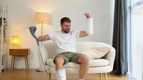A Man with a Broken Hand Foot and Crutch Shows Biceps Dreaming to Return to the Gym