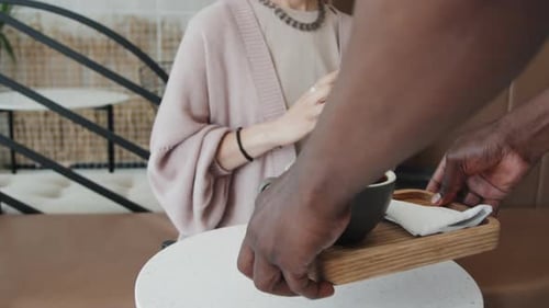 Unerkennbarer Kellner bringt einer kaukasischen Frau ein Tablett mit Kaffee
