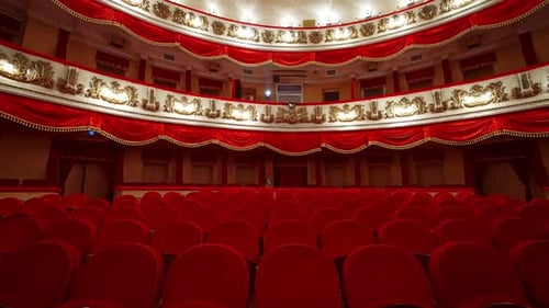 Panoramic view of beautiful richly decorated theater hall. Rows of red chairs in theater hall.