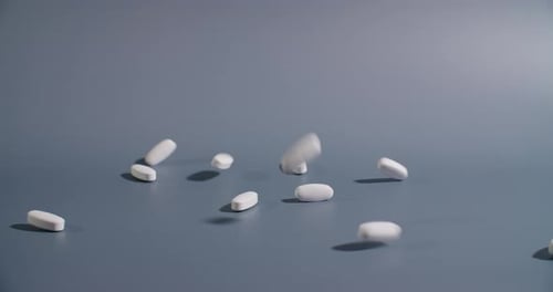 Slow motion close-up of pills falling onto a gray background as they bounce and roll.