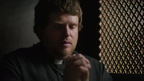 Catholic Priest Talking to Penitent and Praying in Confessional Booth