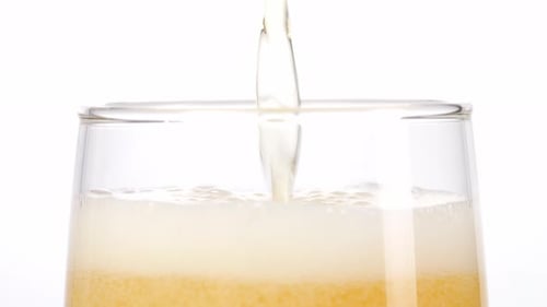 Nahaufnahme von Bier, das in ein Glas auf hellweißem Bildschirmhintergrund im Studio gegossen wird