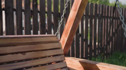 Close Up of Wooden Swing with Chain Beside Second Swing in Sunny Backyard