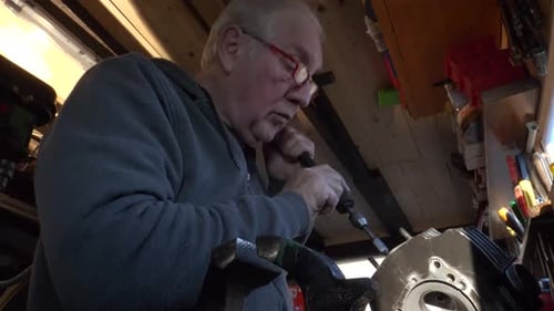 Senior Man Repairs Machine with Drill in Workshop