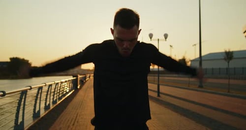 Young Athlete Making Arm Circles Before Training on a City Street at Sunset