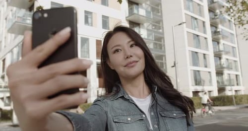 Beautiful Asian woman on video call in city using smart phone