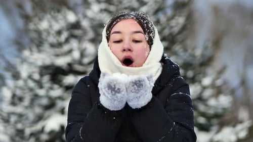 Young Woman Blowing Snow on Winter Day