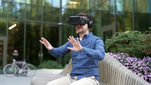 Businessman works using VR glasses in virtual reality simulator sitting on bench on street near