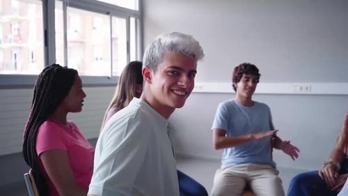 Portrait of Young Man Sitting in Circle Next to His Schoolmates at Class Looking at Camera Smiling