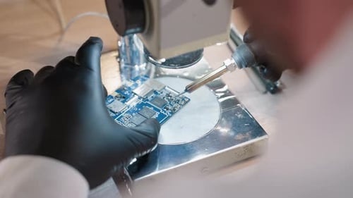 Technician Soldering Circuit Board Under Microscope in Lab