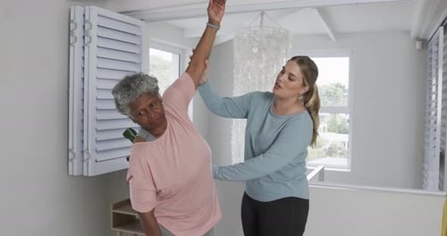 Young Woman Assisting Senior Woman Stretching Indoors