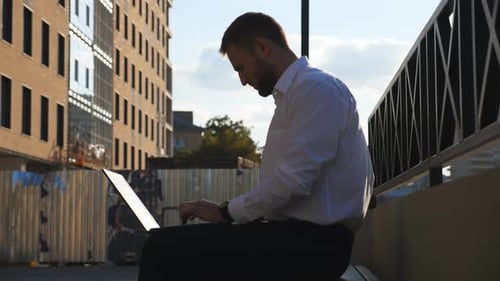 Young Businessman Works on Notebook Sitting on Bench at City