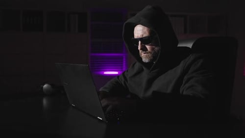 Man in Hoodie Typing on Laptop at Night