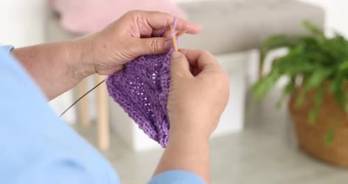 Senior woman knitting with needles at home, closeup
