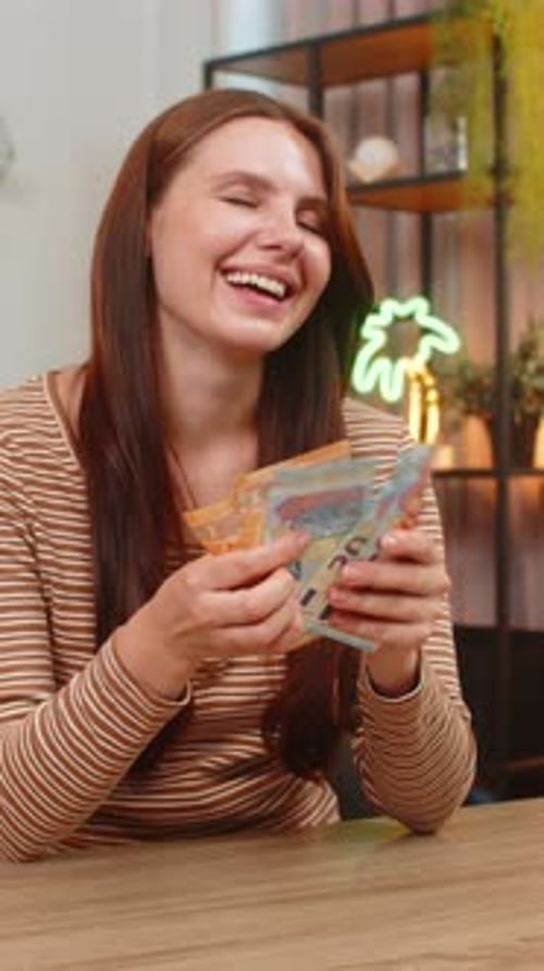 Young Woman Counts Cash Euro Bills at Table Smiles Pleased About Salary Lottery Win Savings Income