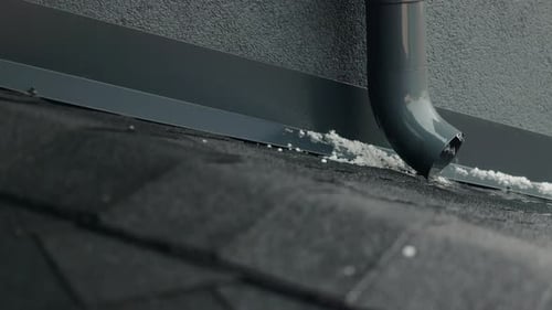 Closeup of Durable Asphalt Shingles Roof with Hail Accumulation Near a Gray Downspout During Rain