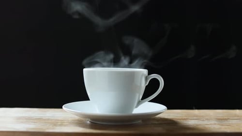 Eine heiße Tasse Kaffee mit Dampf steht auf einem Holztisch auf schwarzem Hintergrund