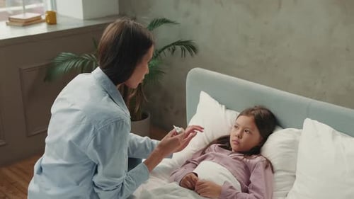 Woman Checks Temperature of Child in Bed