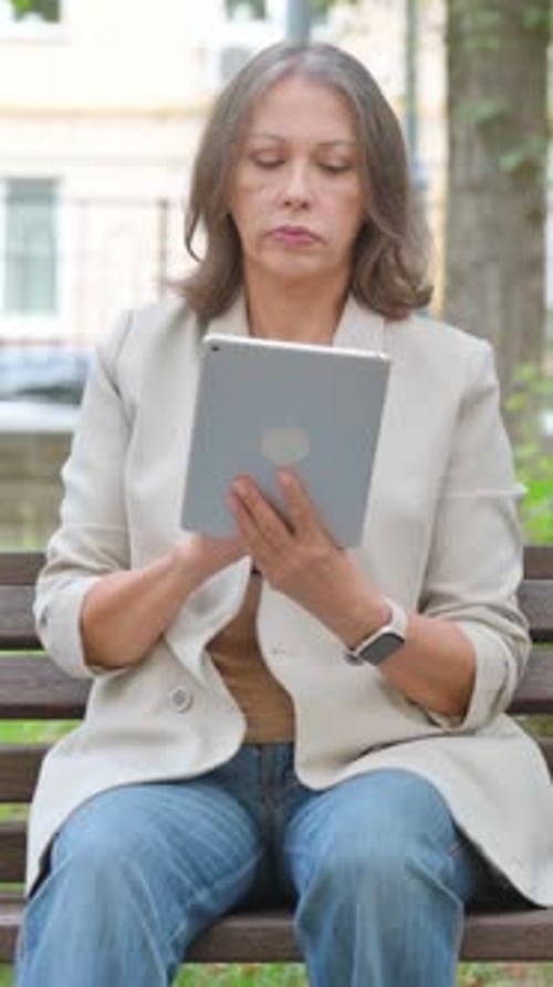 Old Senior Woman Using Digital Tablet while Sitting in Park