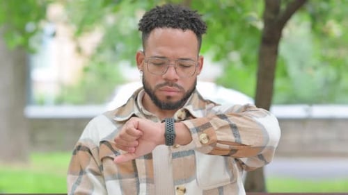 Young Adult Checking Watch While Sitting Outdoors