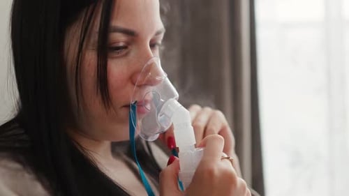 Une femme utilise un nébuliseur pour son traitement respiratoire dans un intérieur serein et calme