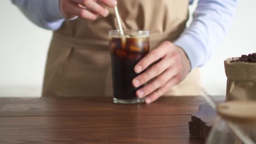 Person Stirring Iced Coffee with a Straw