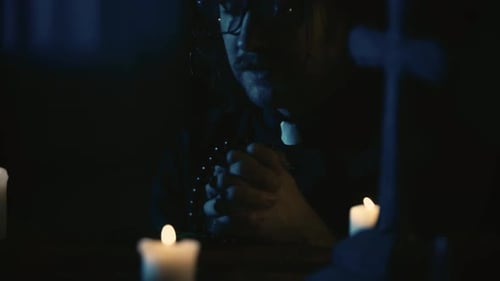 Man Praying in Dark with Candles and Cross
