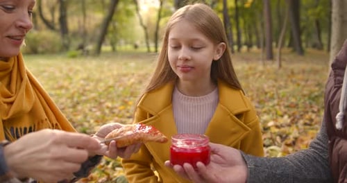 Family Spreads Jam on Croissant in Autumn Park