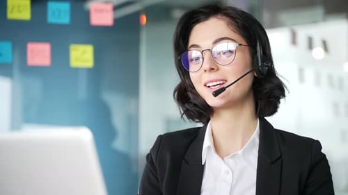 Female customer service representative wearing headset working on laptop in office setting