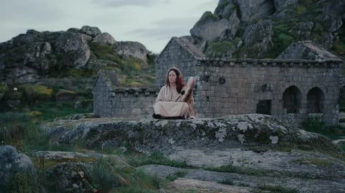 spiritual woman peacefully playing a shamanic drum in a beautiful medieval village track in long sho