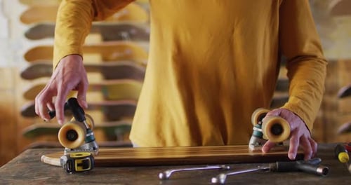 Video of midsection of caucasian male skateboarder fixing skateboard in skate shop