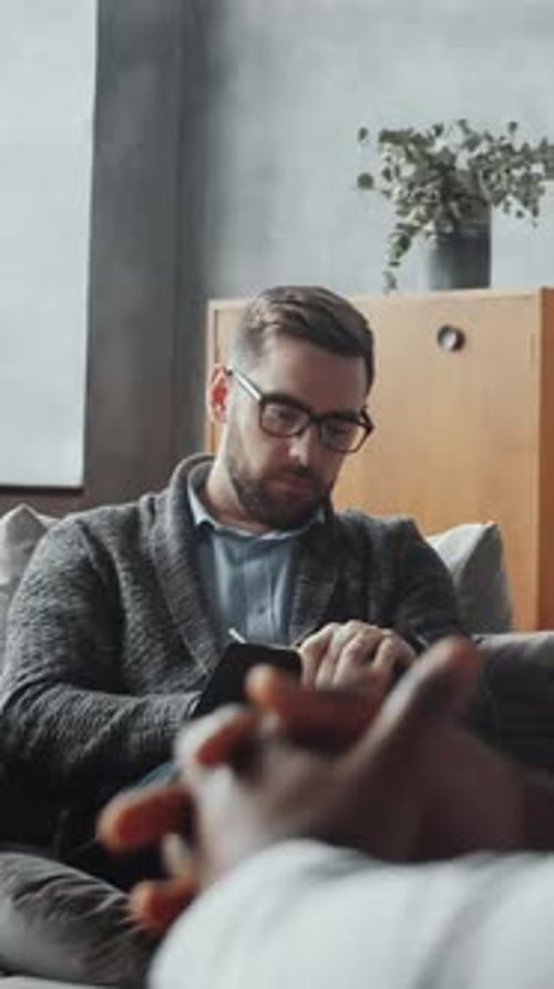 Man in therapy session takes notes on couch