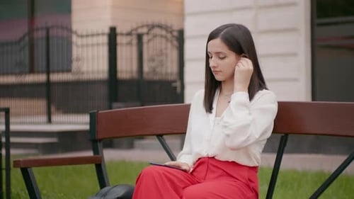 Woman Sits on Bench Using Smartphone in Park