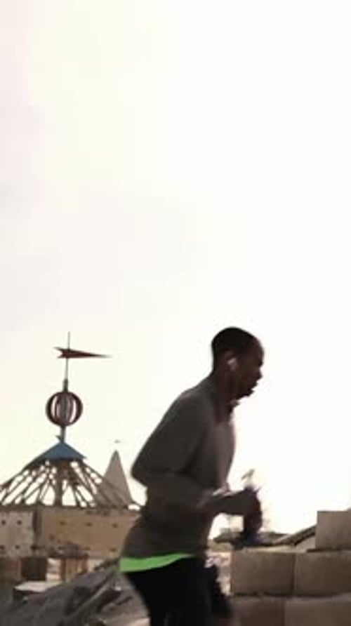 Vertical video: Running man entering frame, crossing sand for training with neon top holding bottle