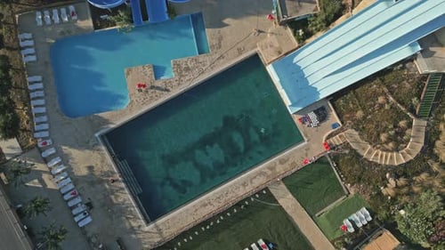 Ascending drone topshot showing water park with swimming pool and slides