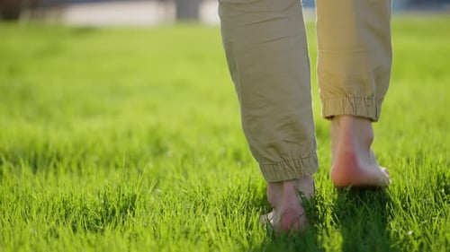 Pés masculinos descalços em transição entre grama verde e concreto, conectando-se ao solo