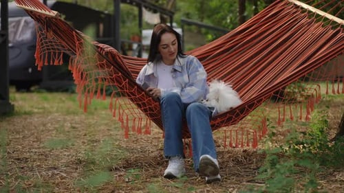 Woman Relaxes with Dog in Hammock with Tablet