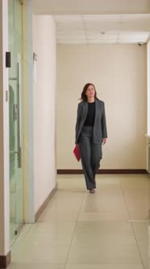 Businesswoman Walking Through Office Hallway with Folder in Hand