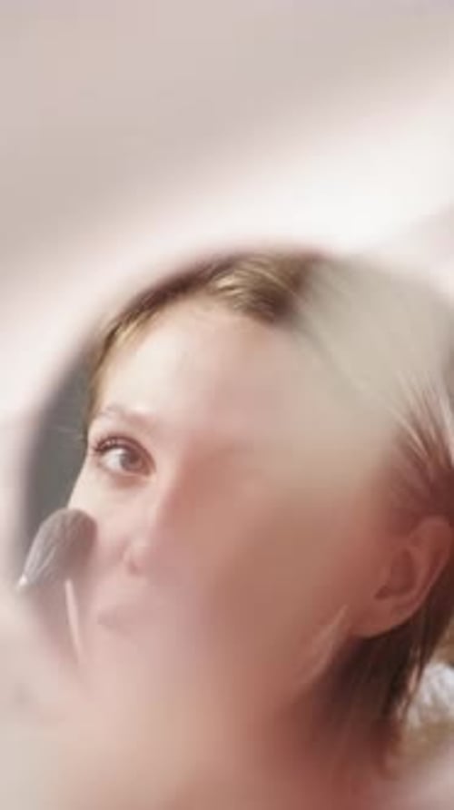 Woman Applying Makeup with Brush in Mirror