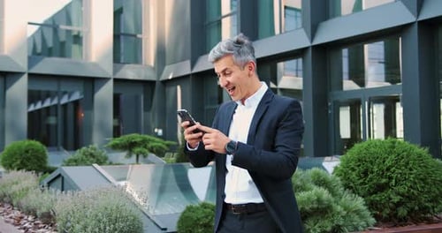 Surprised Businessman in Formal Suit Using a Smartphone in the City and Reacting Emotionally to