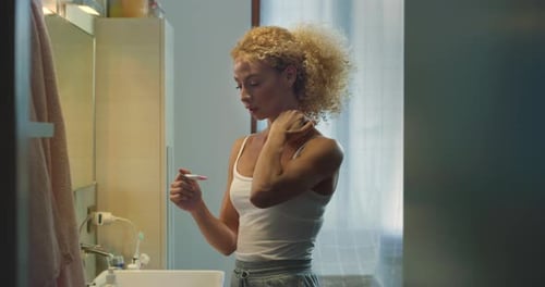 Woman Looks at Pregnancy Test in Bathroom and Smiles
