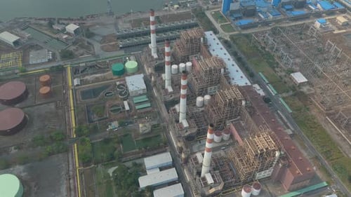 High angle view flying over a massive industrial complex featuring smokestacks, turbines, and