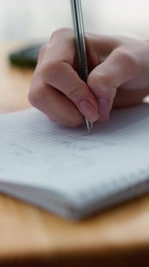 CloseUp of Student Writing on Graph Paper with Coffee and Phone on Table