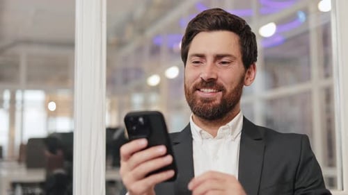 Happy Businessman in Suit Smiles at Phone in Modern Office