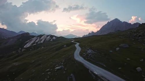 Eine kurvenreiche Bergstraße bei Sonnenuntergang führt durch eine friedliche Landschaft mit fernen Gipfeln.