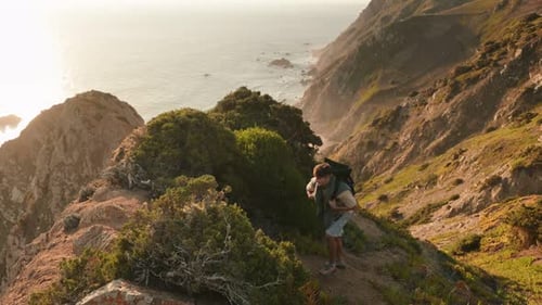 Adventurous Young Man Hiking Steep Hill By Ocean at Sunset