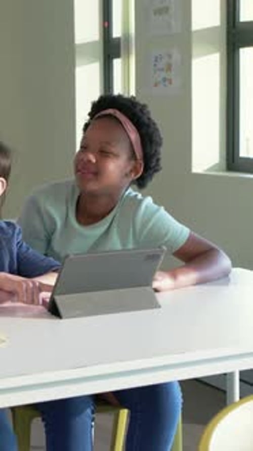 Student pointing at tablet, students working at white table, teacher approaching and guiding math