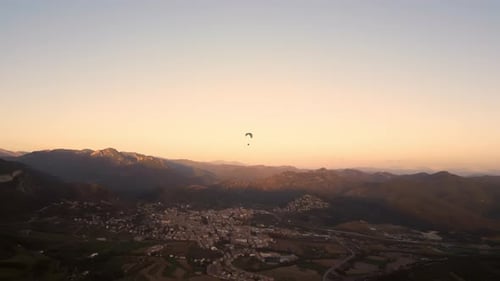 Paraglider Soaring Over Town and Valley at Sunset