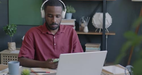 Carefree Businessman Listening to Music Through Headphones and Working with Laptop in Office