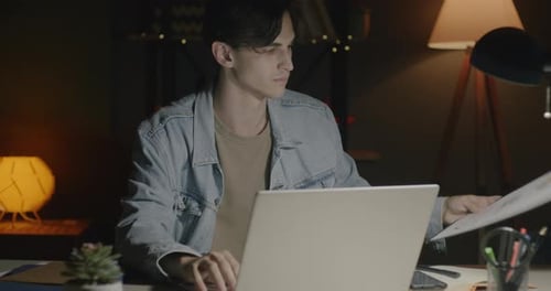 Motivated Employee Working in Office at Night Using Laptop and Checking Business Documents